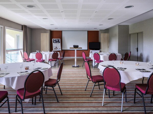 A conference room with multiple tables, chairs, a projector screen, and a television.
