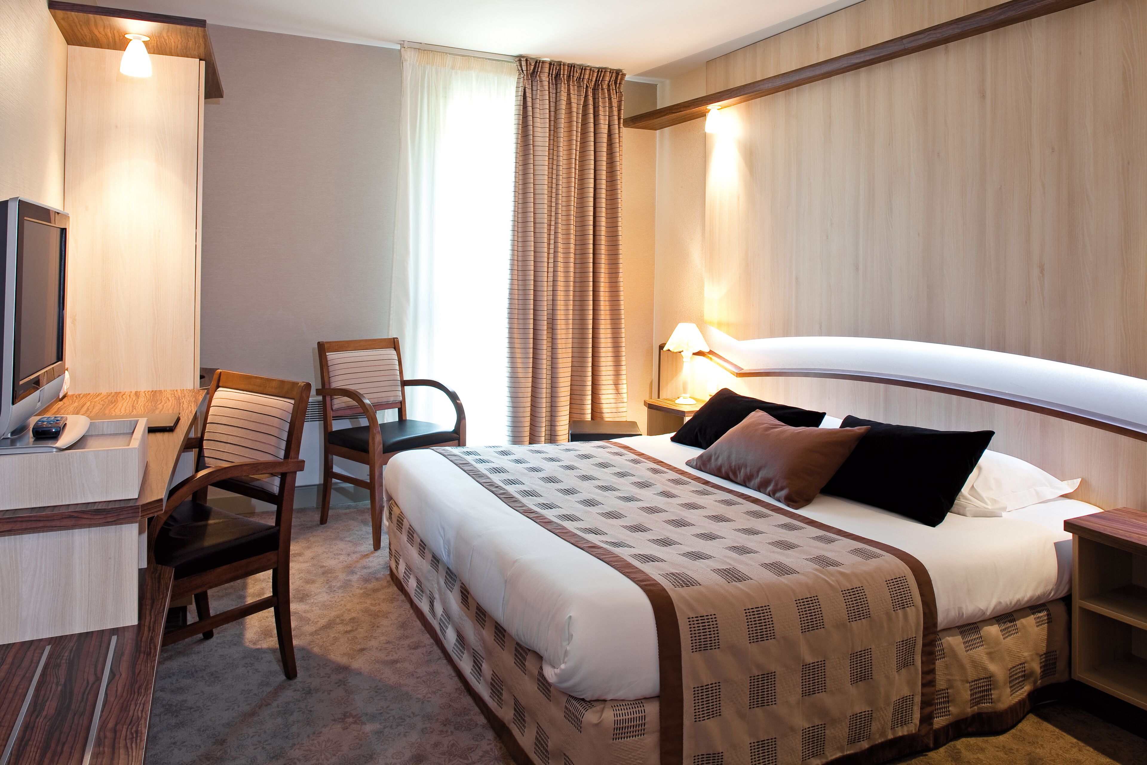 Una habitación de hotel con cama, escritorio, silla, televisor y lámpara.