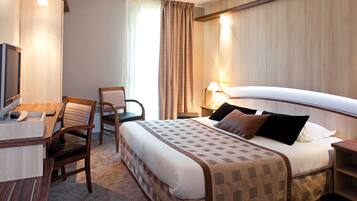 Una habitación de hotel con cama, escritorio, silla, televisor y lámpara.