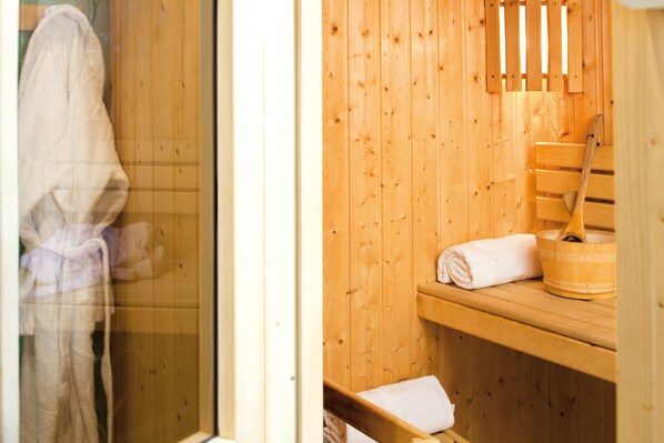 A wooden sauna with a bench, a wooden bucket, and a towel on the bench.