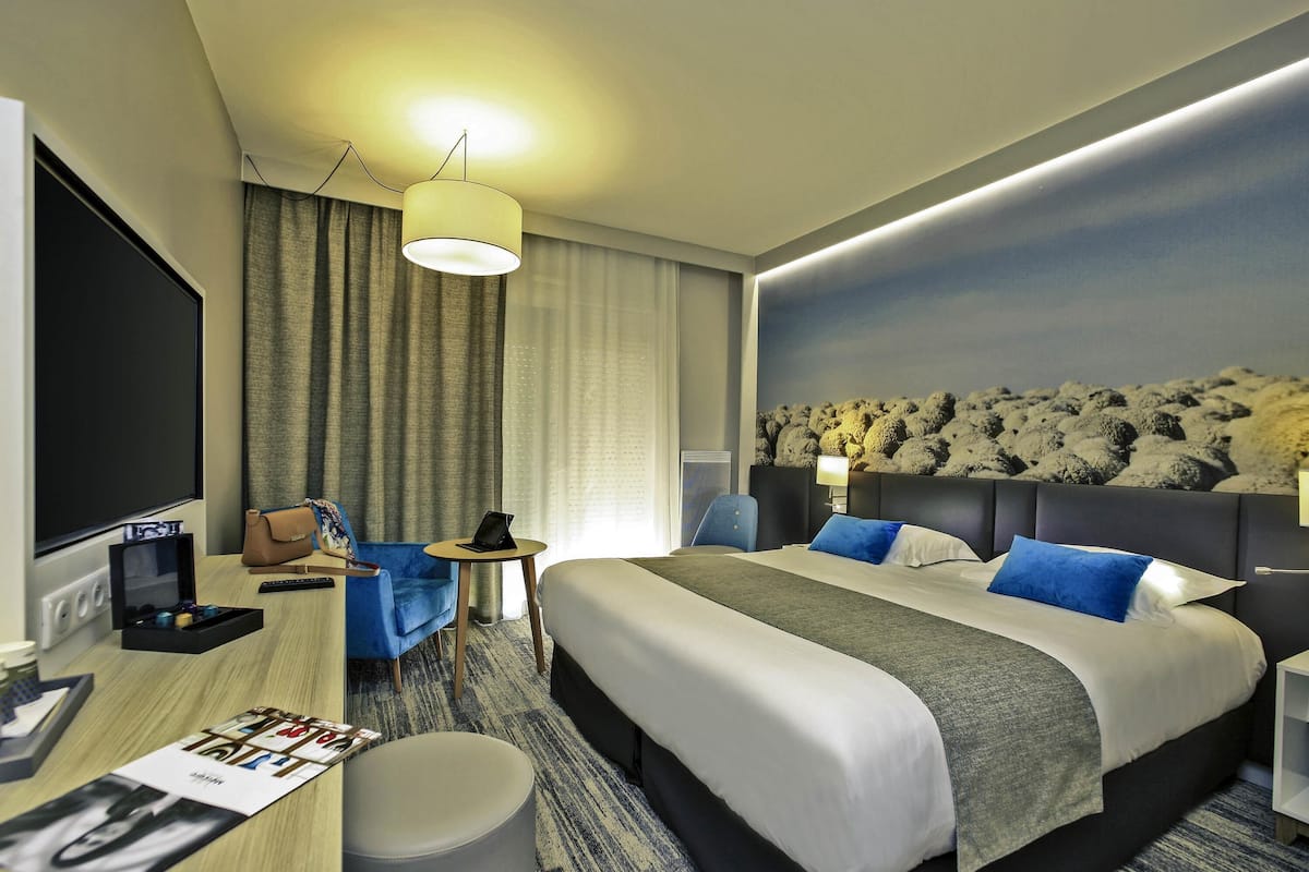 A hotel room with a large bed, a desk with a computer, a chair, and a TV.
