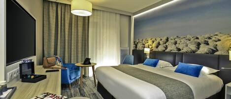 A hotel room with a large bed, a desk with a computer, a chair, and a TV.