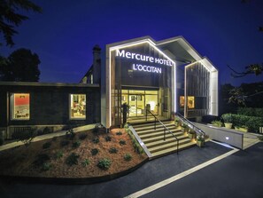 A modern hotel with a prominent entrance, a staircase leading to the lobby, and a well-lit facade.