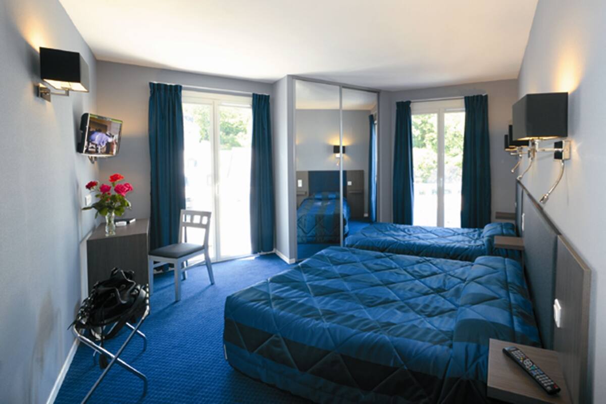 Hotelkamer met twee bedden, een bureau, een stoel, een televisie en een raam met gordijnen.