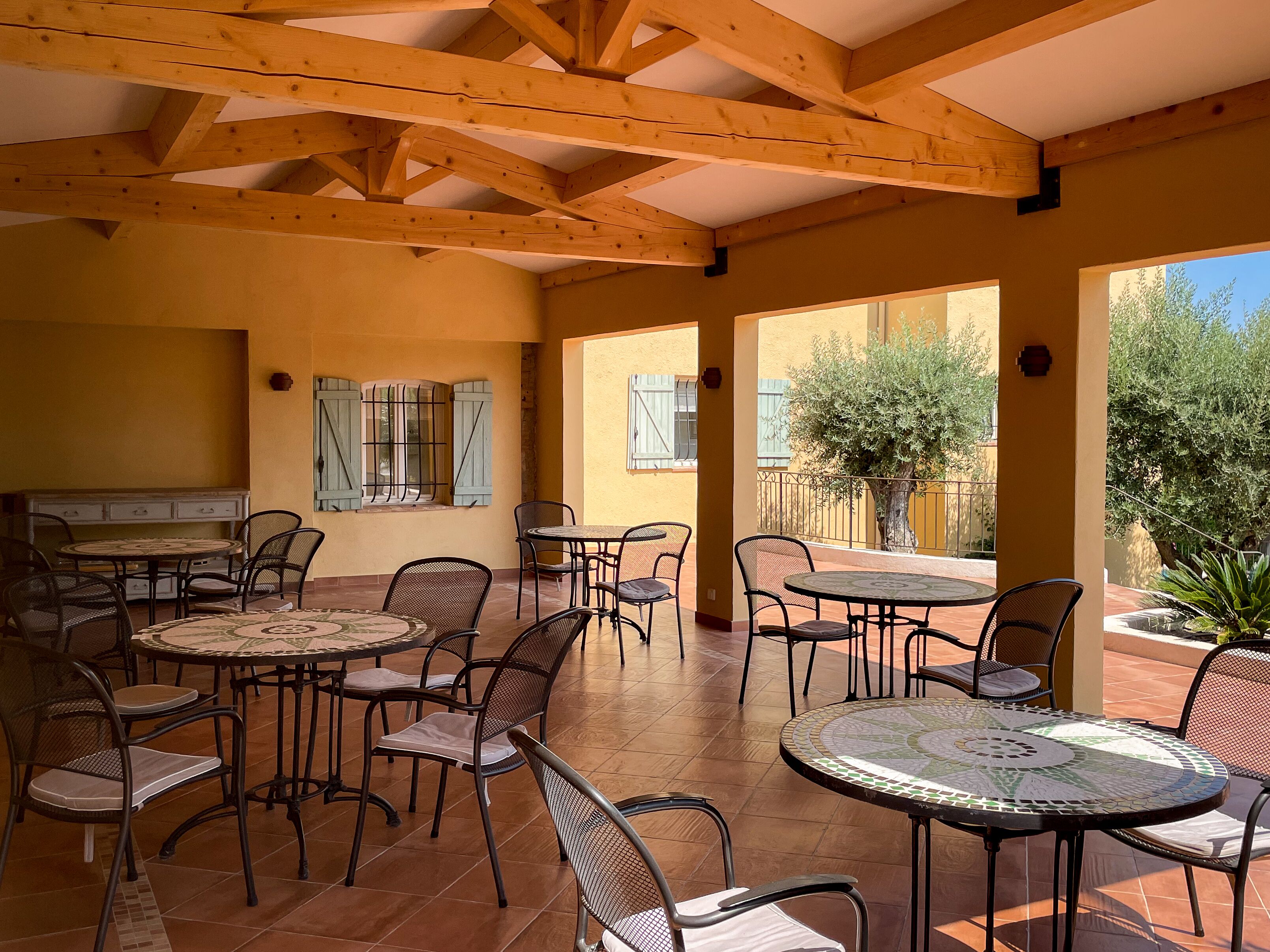 An outdoor patio with wooden beams, tiled flooring, and multiple round tables and chairs.
