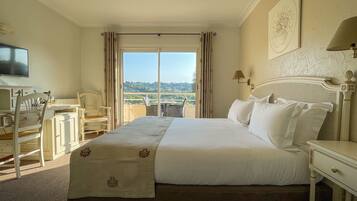 Une chambre d’hôtel équipée d’un lit, d’un bureau, d’une chaise, d’une télévision et d’un balcon avec vue.