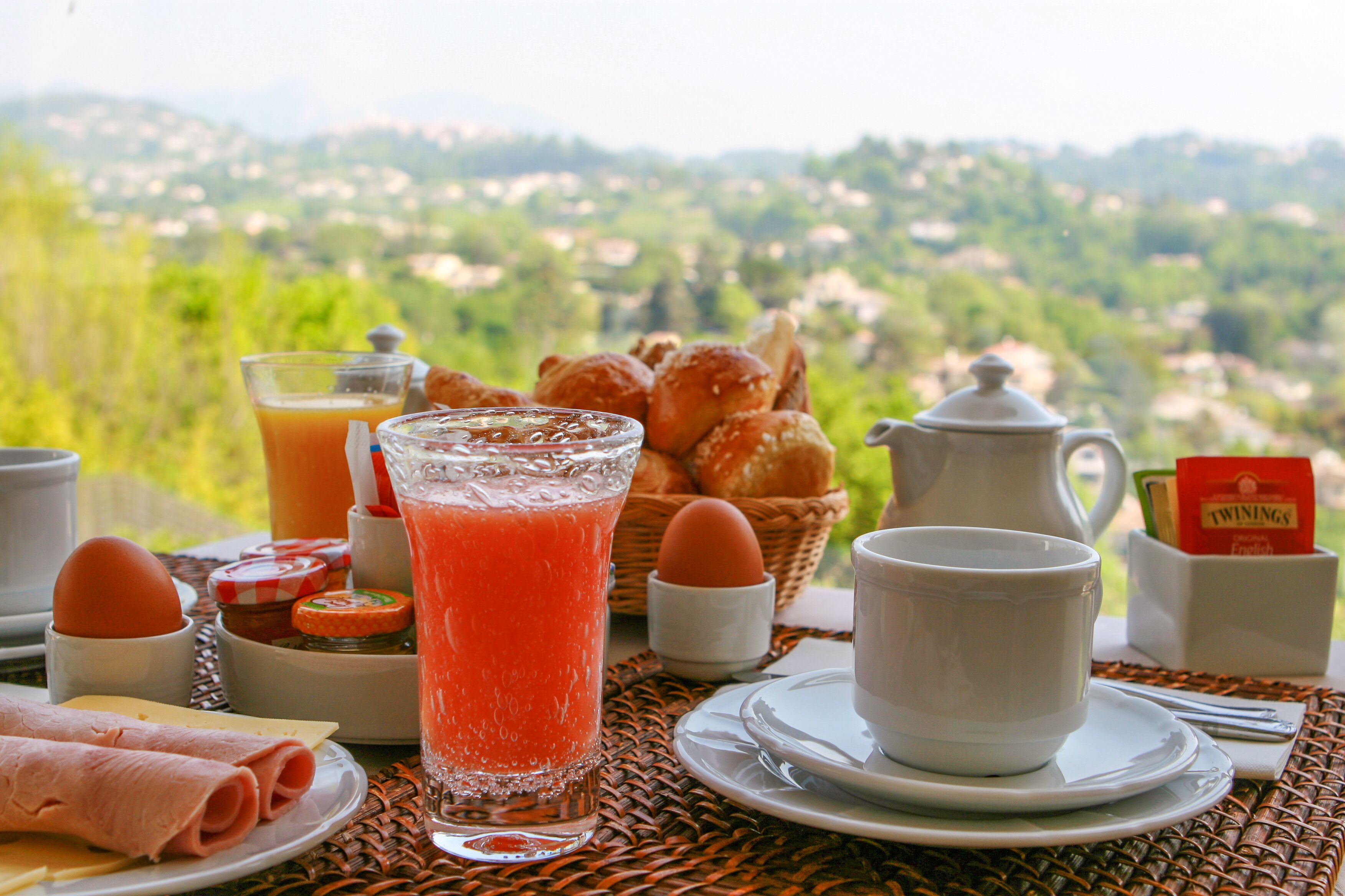 A breakfast table with croissants, a glass of orange juice, and a view of a green landscape.