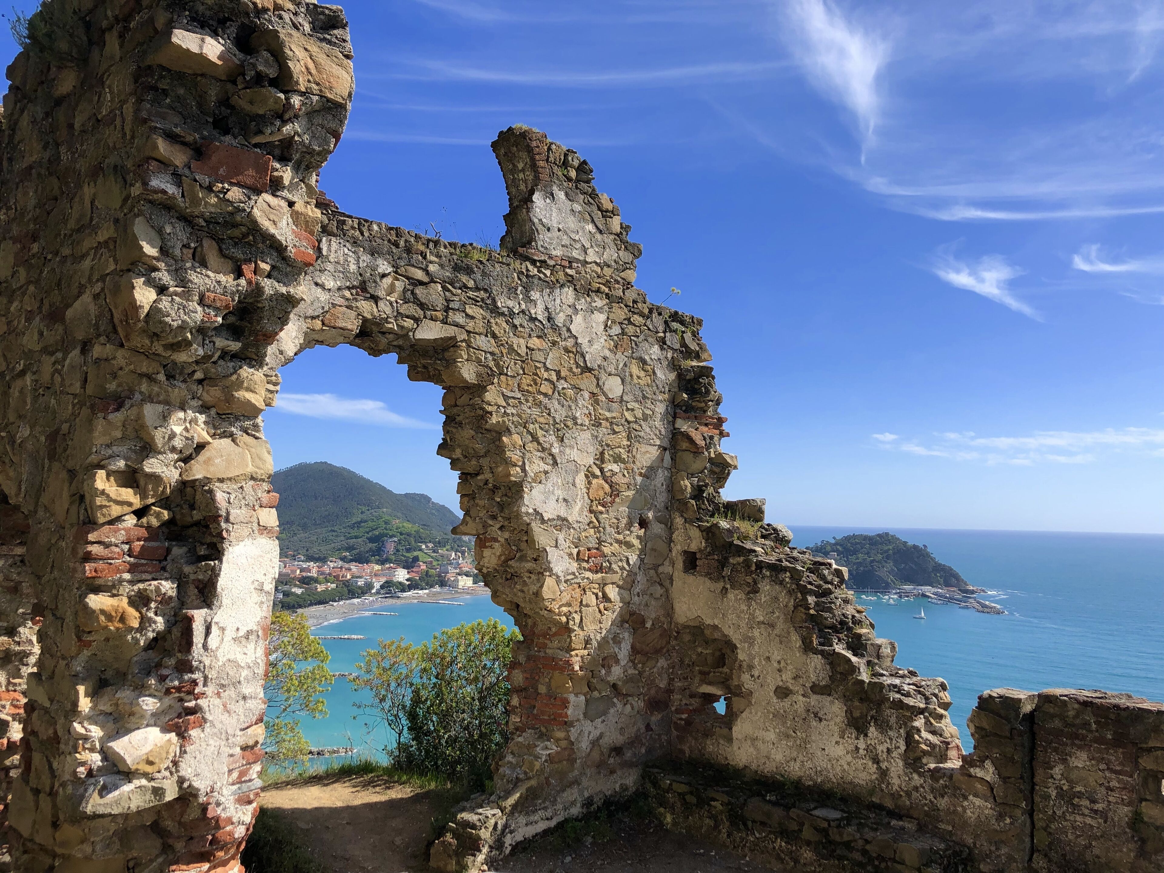 An ancient stone archway leading to a coastal town with a view of the sea and mountains.