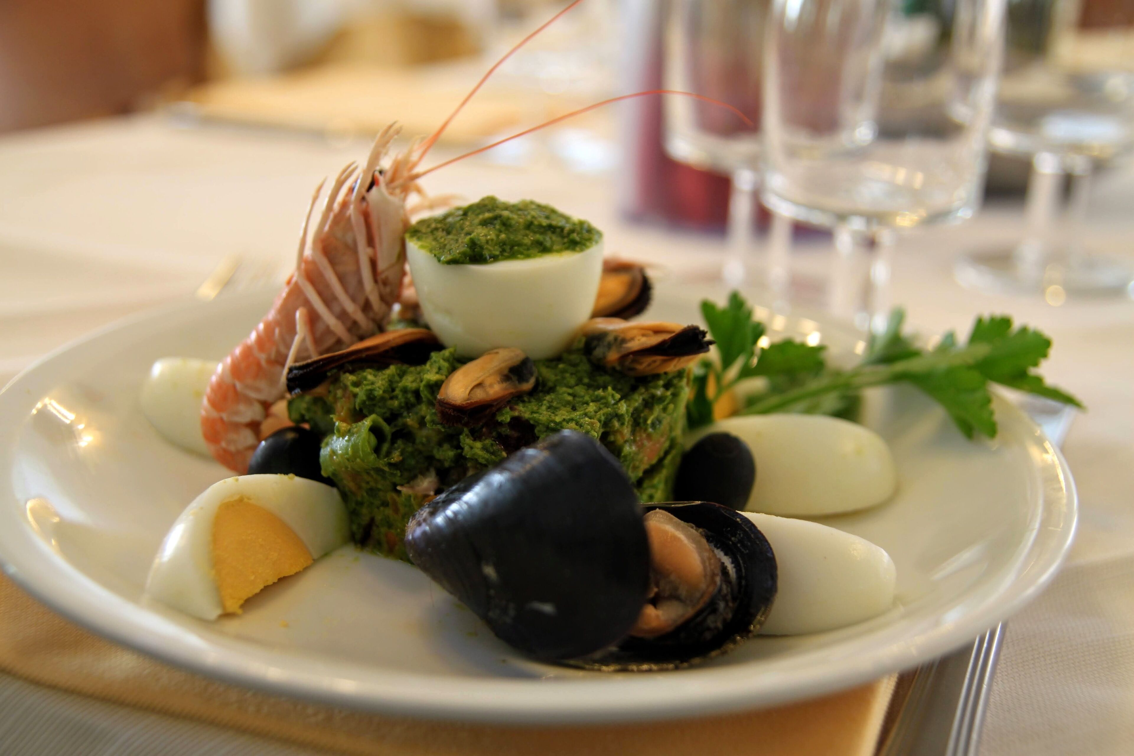 A seafood dish with mussels, shrimp, and a green sauce on a white plate.