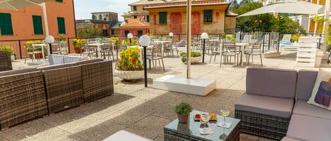 An outdoor patio with wicker furniture, a glass-top table, and umbrellas providing shade.