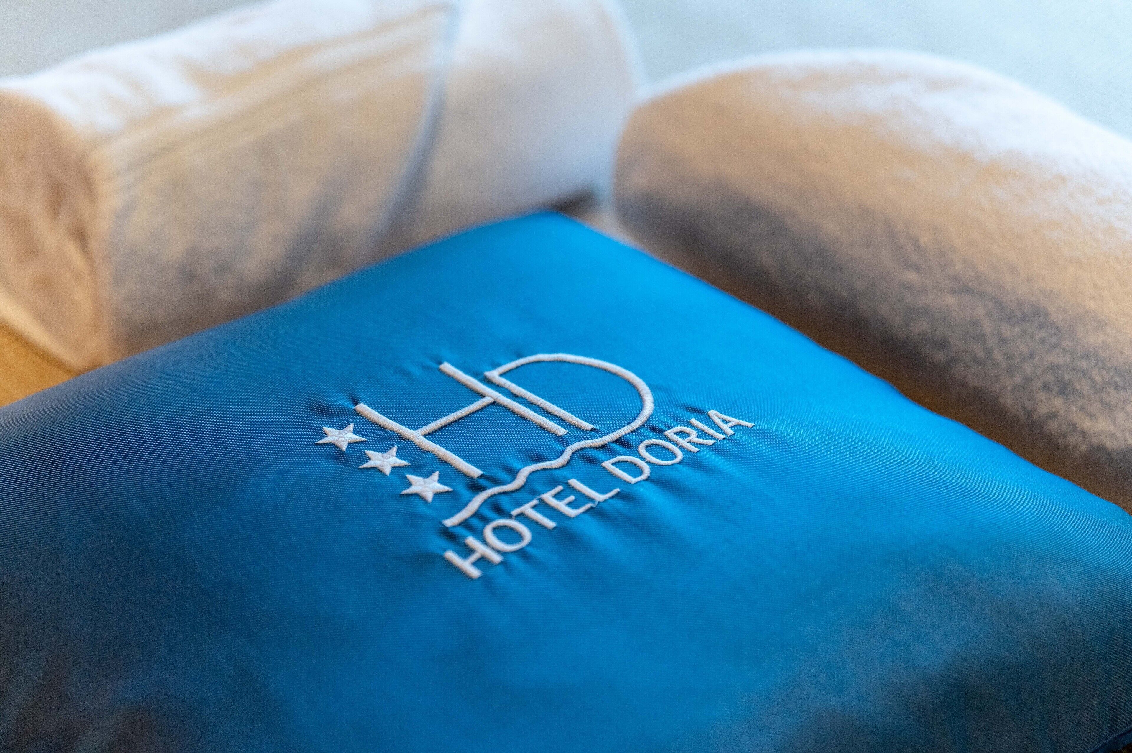 Ein blaues Kissen mit eingesticktem Logo "HD HOTEL DORIA".