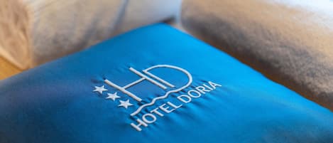 A blue pillow with the logo "HD HOTEL DORIA" embroidered on it.