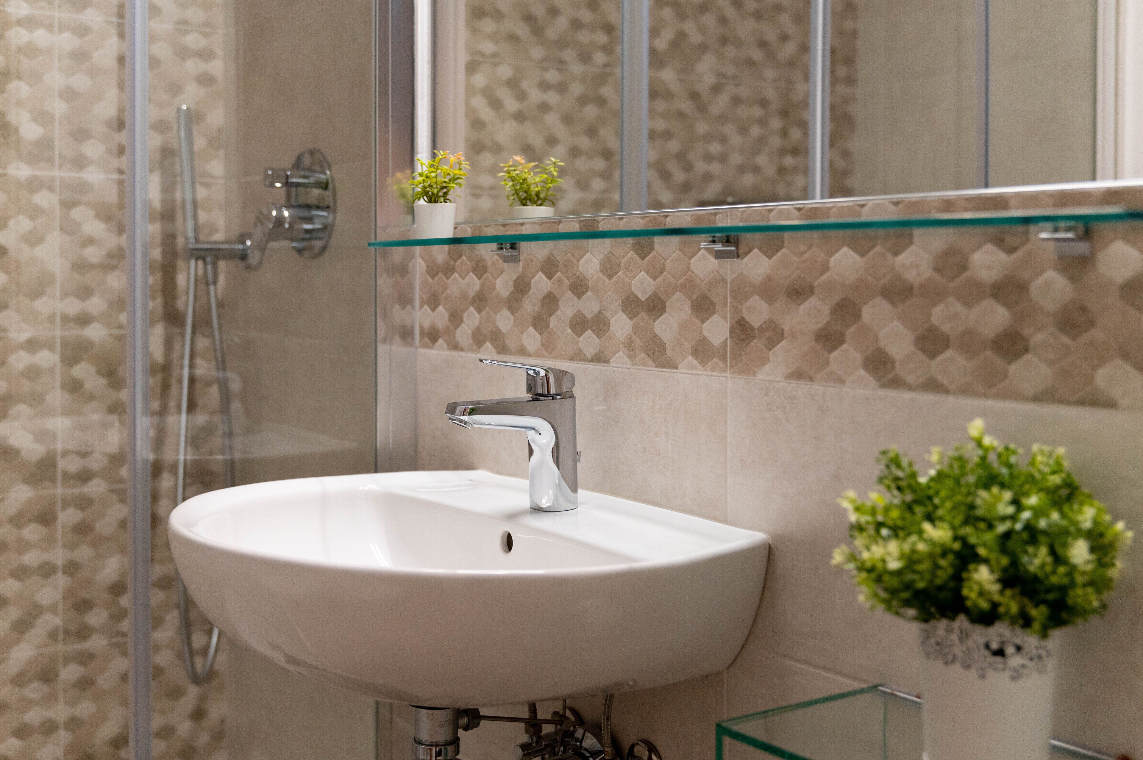Un baño con cabina de ducha de vidrio, un lavabo blanco y un espejo encima.