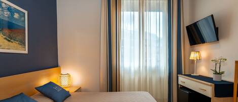 A hotel room with a bed, a desk, a TV, and a window with curtains.