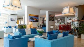 Un salón moderno con sofás azules, una mesa de centro y plantas decorativas. Cuenta con una zona de cocina con detalles en rojo y una escalera.