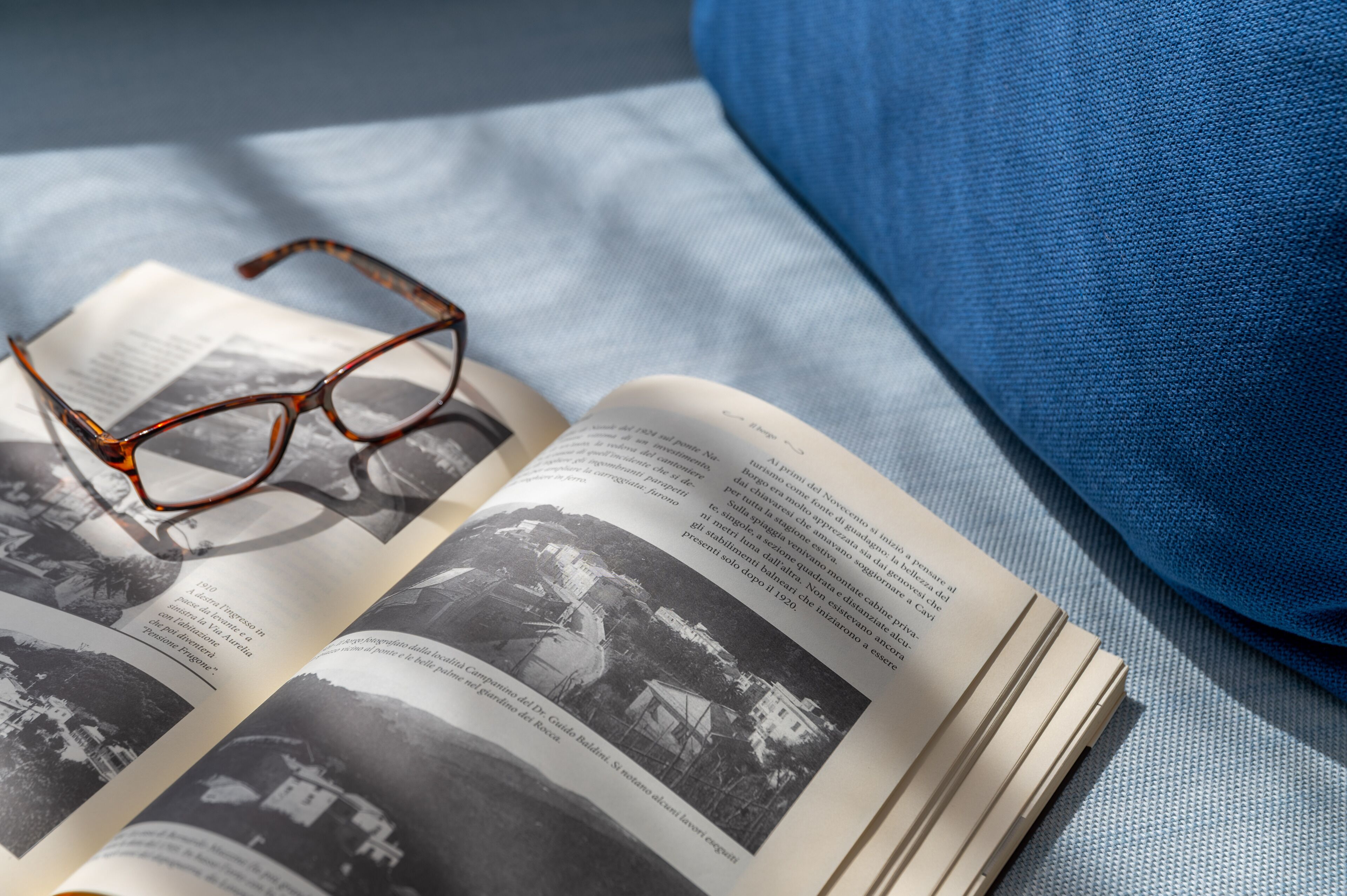 Ein offenes Buch mit Brille darauf, auf einer blauen Stoffunterlage platziert.