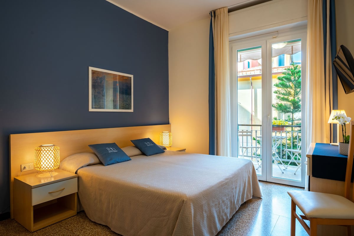 A neatly arranged bedroom with a bed, bedside lamps, a small table, and a chair.