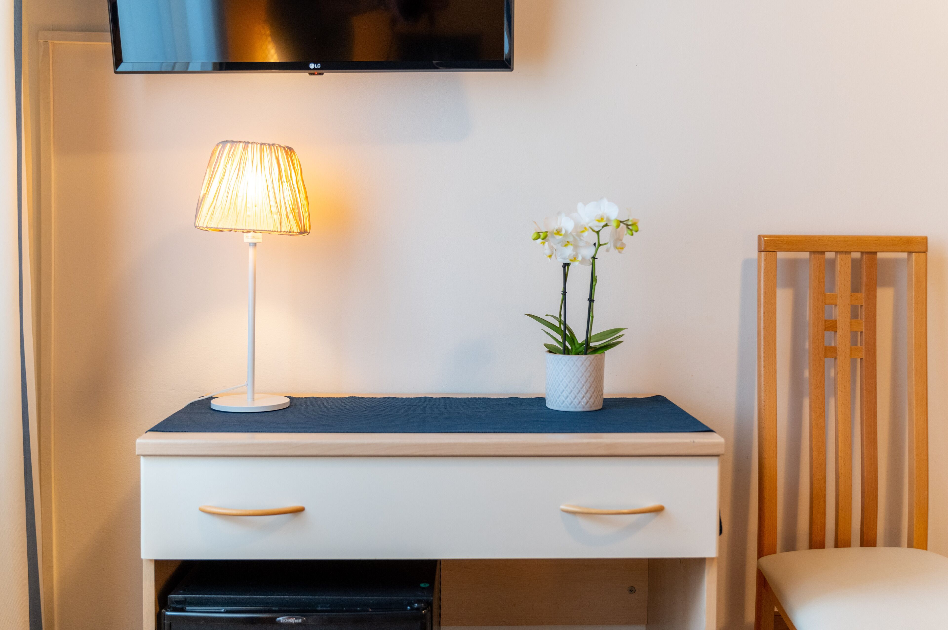 Un bureau avec une lampe, une plante en pot et un téléviseur fixé au mur.