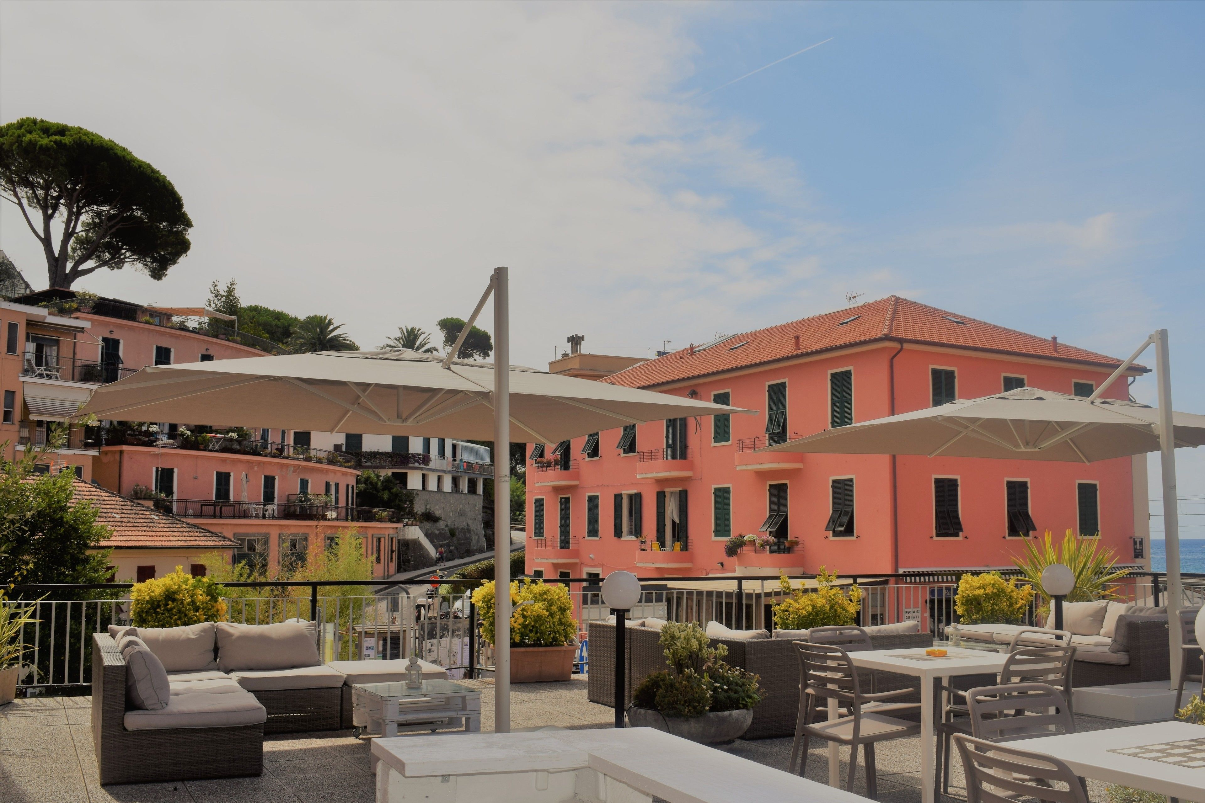 A rooftop terrace with outdoor seating, a view of a pink building, and a large tree.