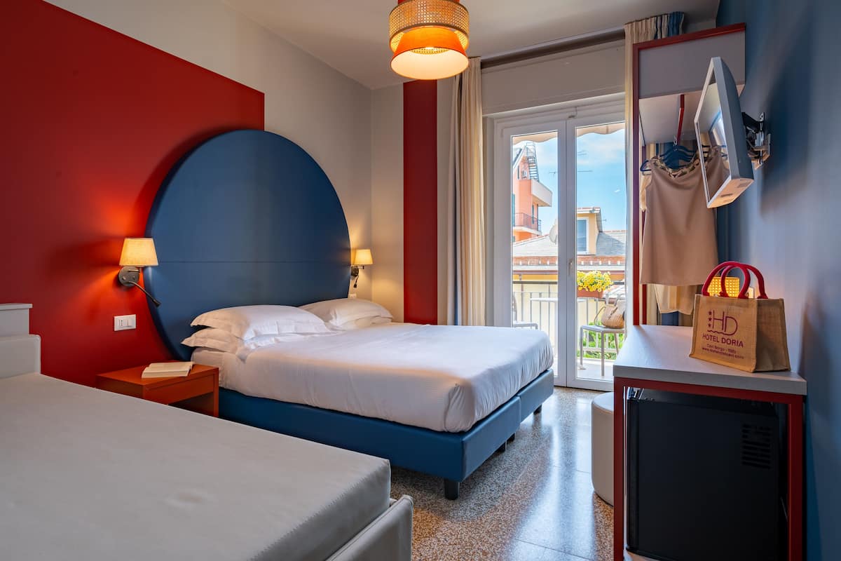 A hotel room with a bed, bedside tables, a lamp, a TV, and a view of the outside.