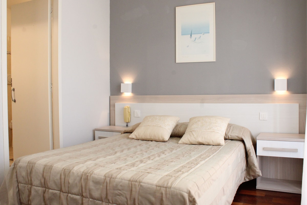 Un dormitorio con cama, mesitas de noche, lámpara de pared e imagen enmarco.