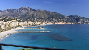 A coastal city with a beach, rocky outcrops, and a mountain in the background. - Hôtel Alexandra (Roquebrune-Cap-Martin)