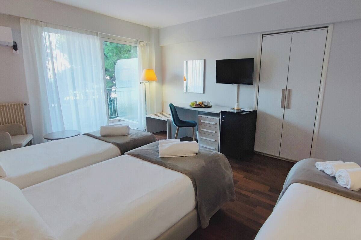 Hotellihuone, jossa on kaksi sänkyä, työpöytä tuolilla, televisio ja ikkuna, jossa on verhot.
