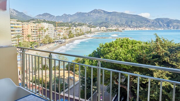 A balcony with a view of a beach, ocean, and mountains. - Hôtel Alexandra (Roquebrune-Cap-Martin)
