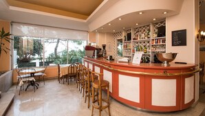 A bar area with a curved counter, bar stools, and a view of the outdoors. - Hôtel Alexandra (Roquebrune-Cap-Martin)