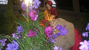 A statue of a person in traditional attire surrounded by purple orchids.