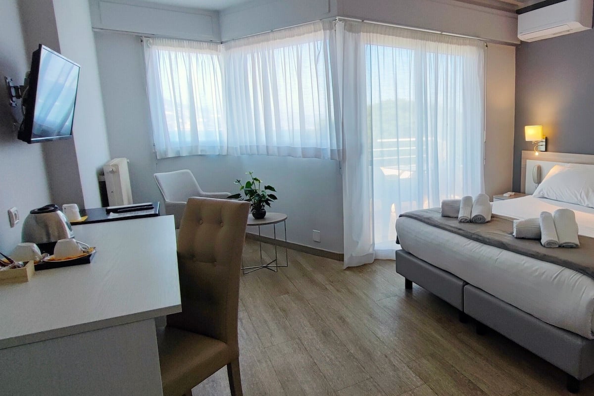Hotellihuone, jossa on sänky, yöpöydät, työpöytä, tuoli ja televisio.