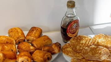 A buffet with various pastries, including croissants and rolls, and a bottle of maple syrup.