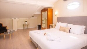 A hotel room with a large bed, a bedside table, a chair, and a small table with a vase of flowers. - Hotel Les Armoiries (Valbonne)