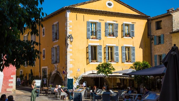 A yellow building with blue shutters, outdoor seating, and a sign that reads "mouilleries." - Hotel Les Armoiries (Valbonne)