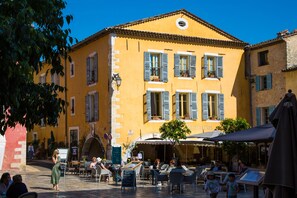 A yellow building with blue shutters, outdoor seating, and a sign that reads "mouilleries." - Hotel Les Armoiries (Valbonne)