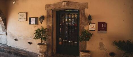 A hotel entrance with a stone archway, a signboard, and two potted plants.