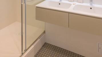 Une salle de bain moderne avec une douche à parois de verre, un grand miroir et un meuble-lavabo blanc doté de deux vasques.