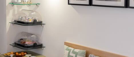 Un comedor con mesas dispuestas para el desayuno, una estación de café y estantes en la pared con alimentos.