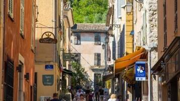 Una calle empedrada flanqueada por edificios históricos, un café y una tienda con terraza.