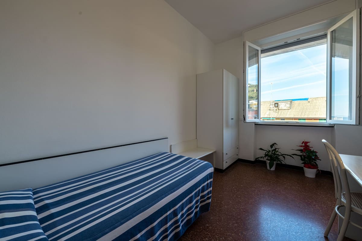 A small, sparsely furnished room with a bed, a desk, and a window.