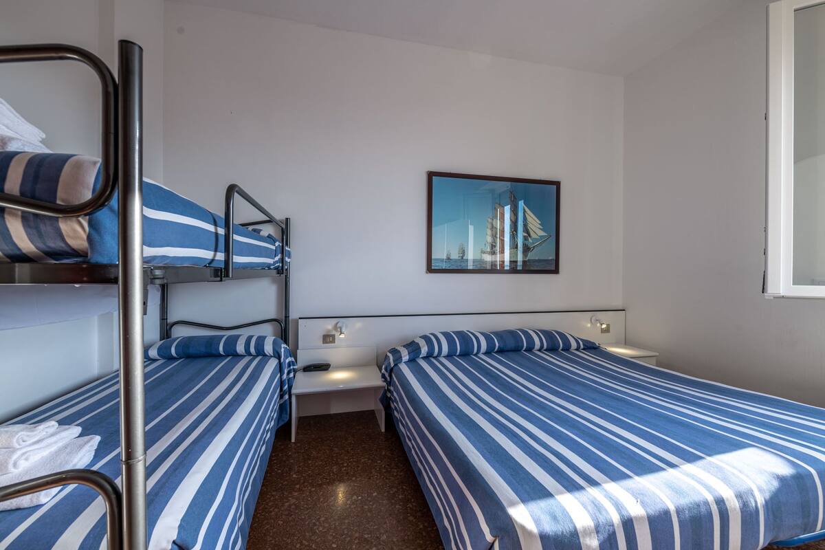 A hotel room with bunk beds, a small bedside table, a nightstand, and a framed picture on the wall.