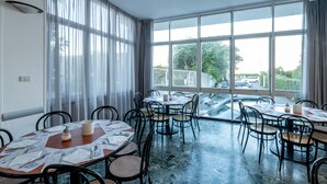 Un comedor con mesas dispuestas para cuatro, ventanas amplias con cortinas, y vista a la calle.