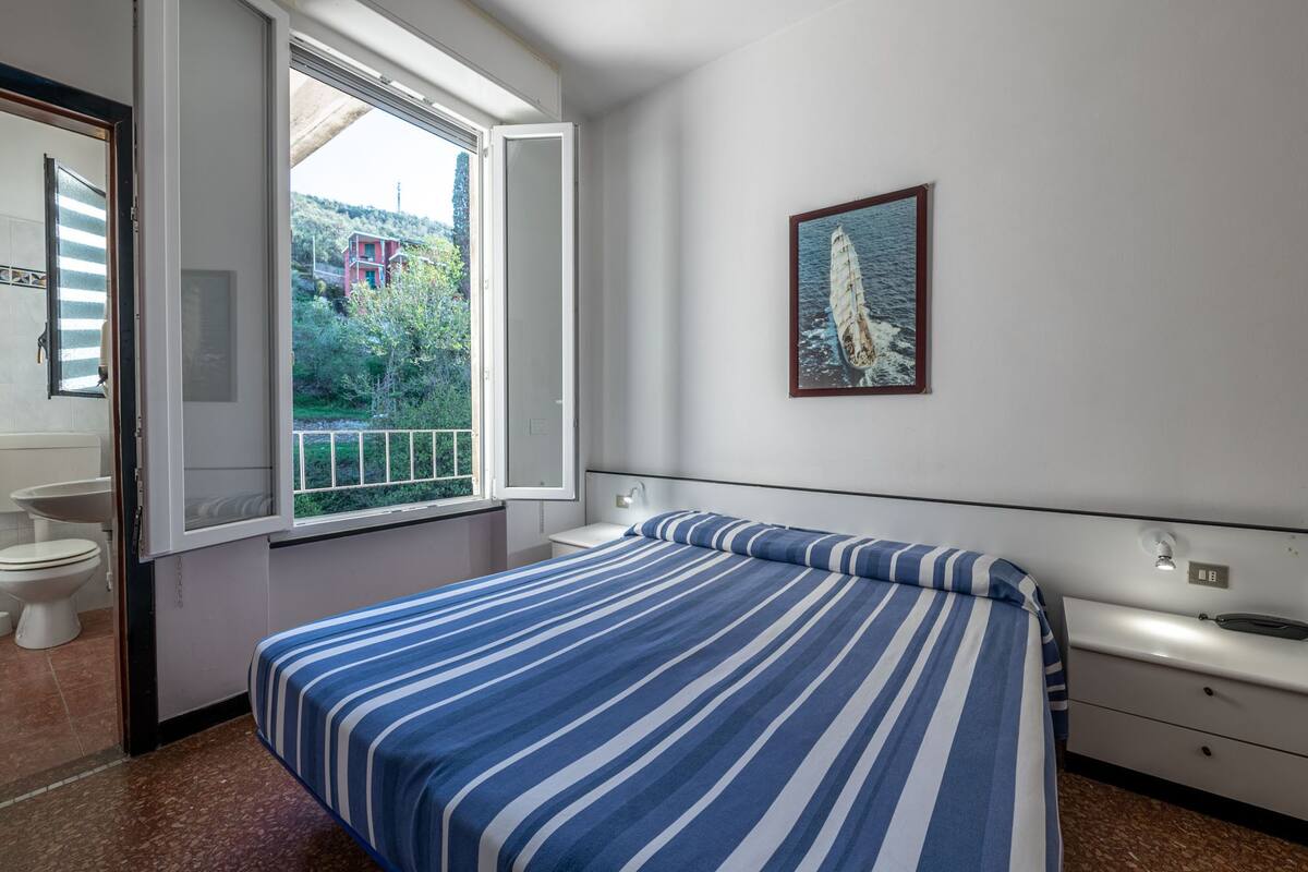 A bedroom with a bed, a window, a sink, and a painting on the wall.