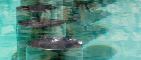 A series of cylindrical objects in a reflective surface, possibly a pool or water feature.
