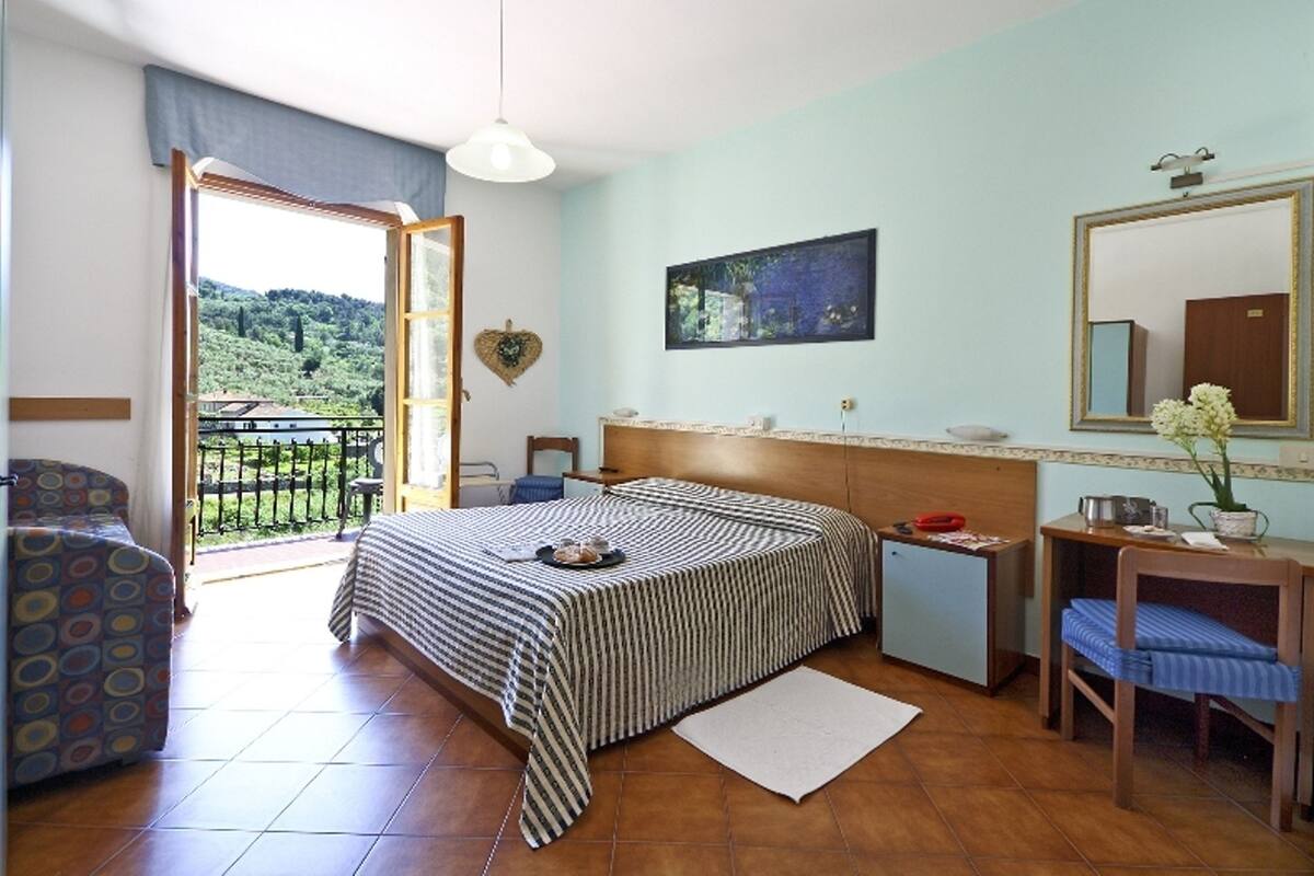 Un dormitorio con cama, escritorio, silla, espejo y vistas al exterior.