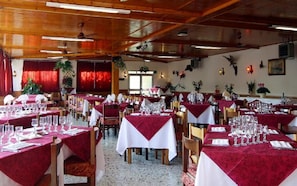 A restaurant with multiple tables set for dining, featuring red and white tablecloths and wooden chairs. - Hotel San Matteo (San Bartolomeo al Mare)