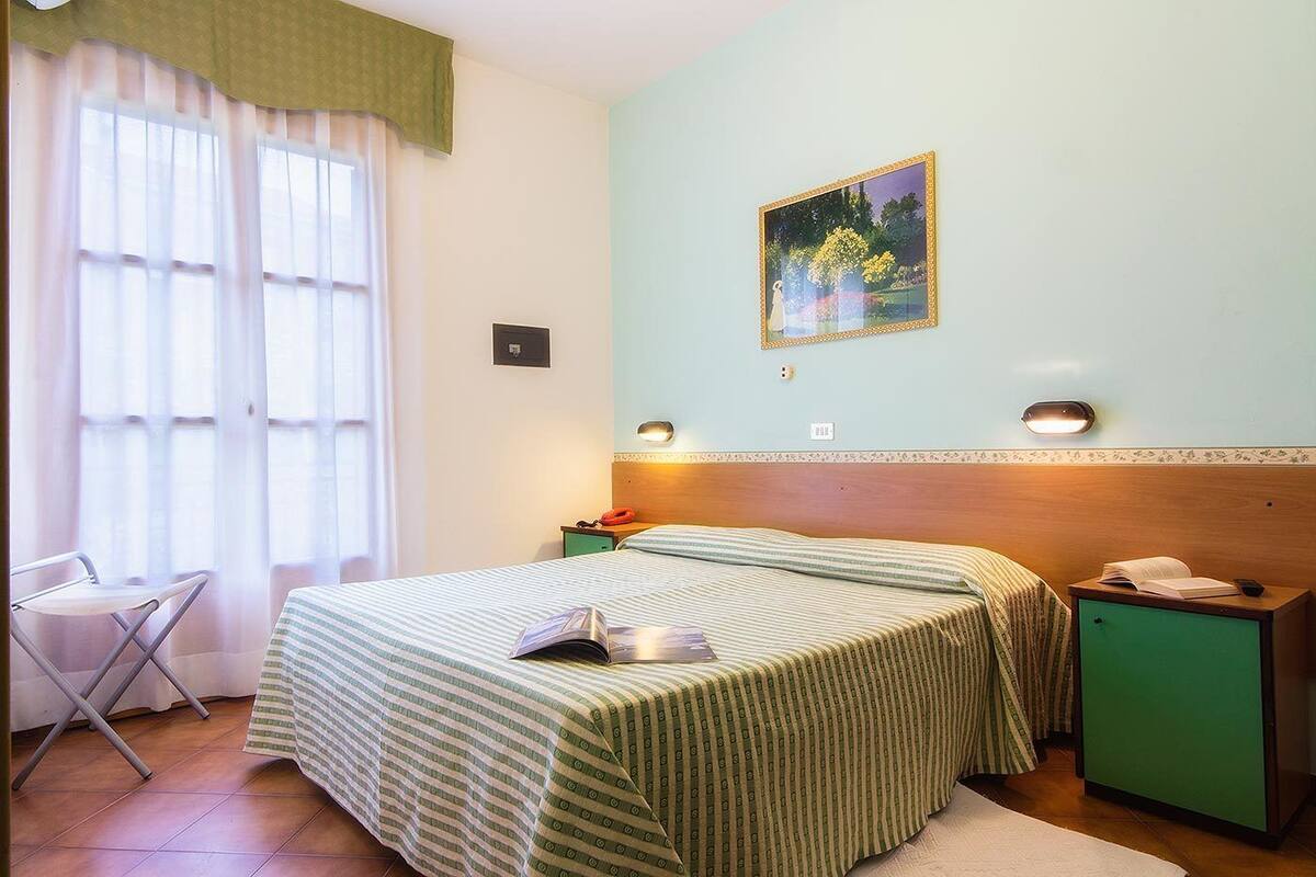 Un dormitorio con una cama, una silla, una mesita de noche y un cuadro en la pared.