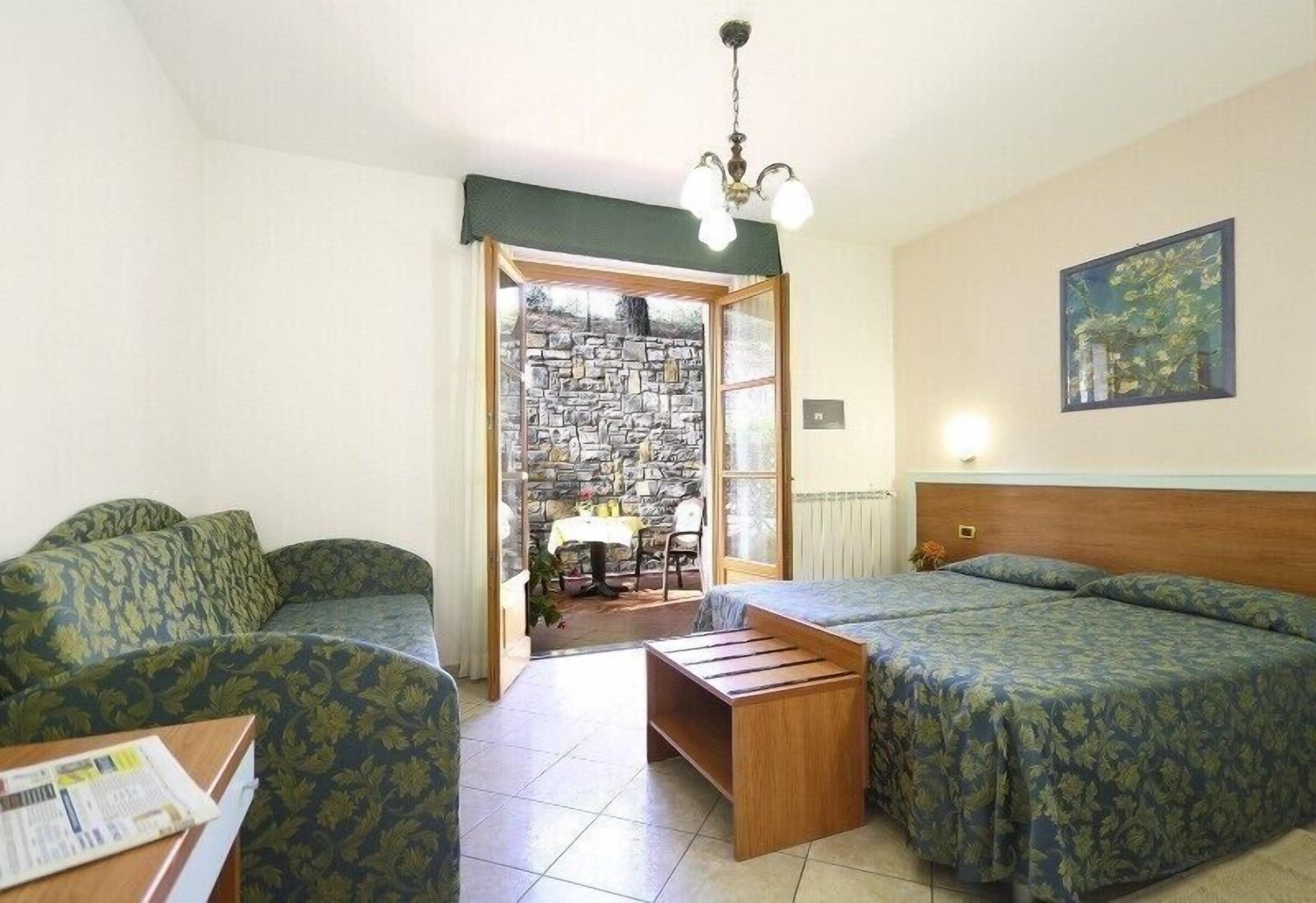Una habitación con dos camas, una mesa de madera y una silla. Se ve una pared de piedra a través de una puerta de cristal.