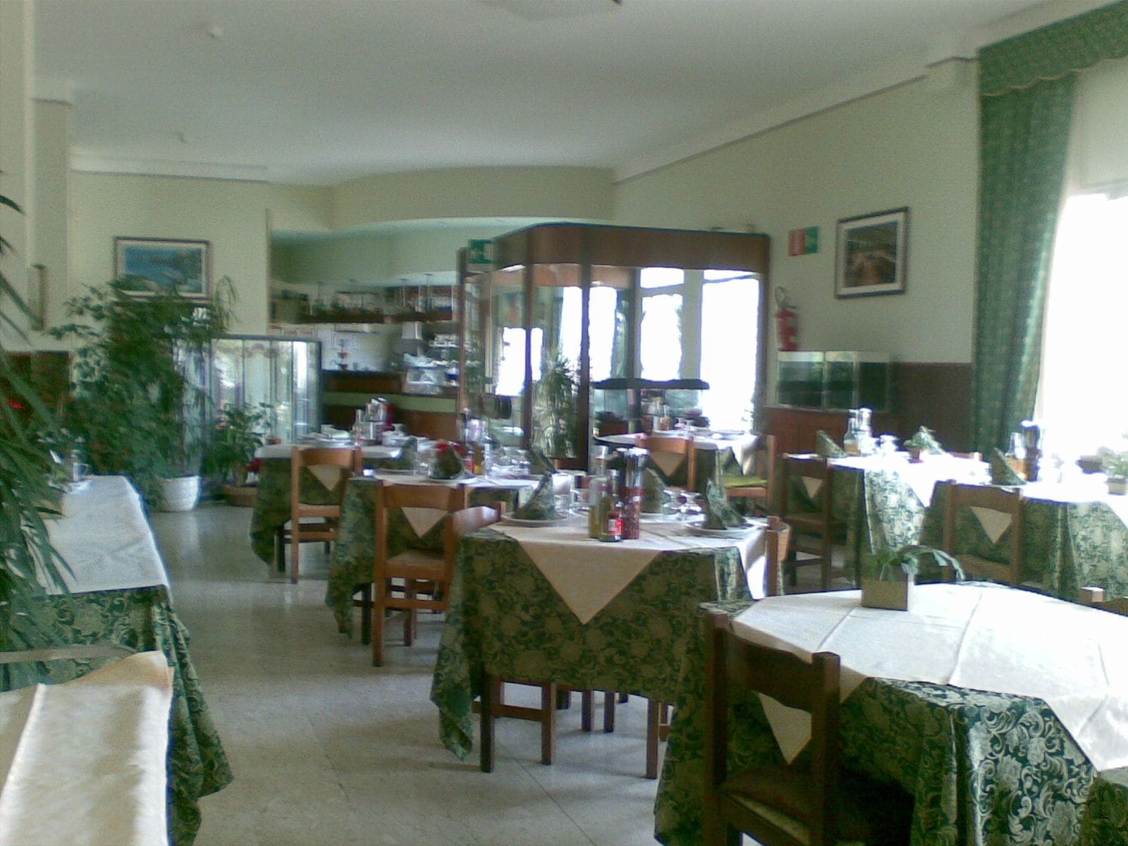 A dining area with tables set for a meal, chairs, and a large window providing natural light.