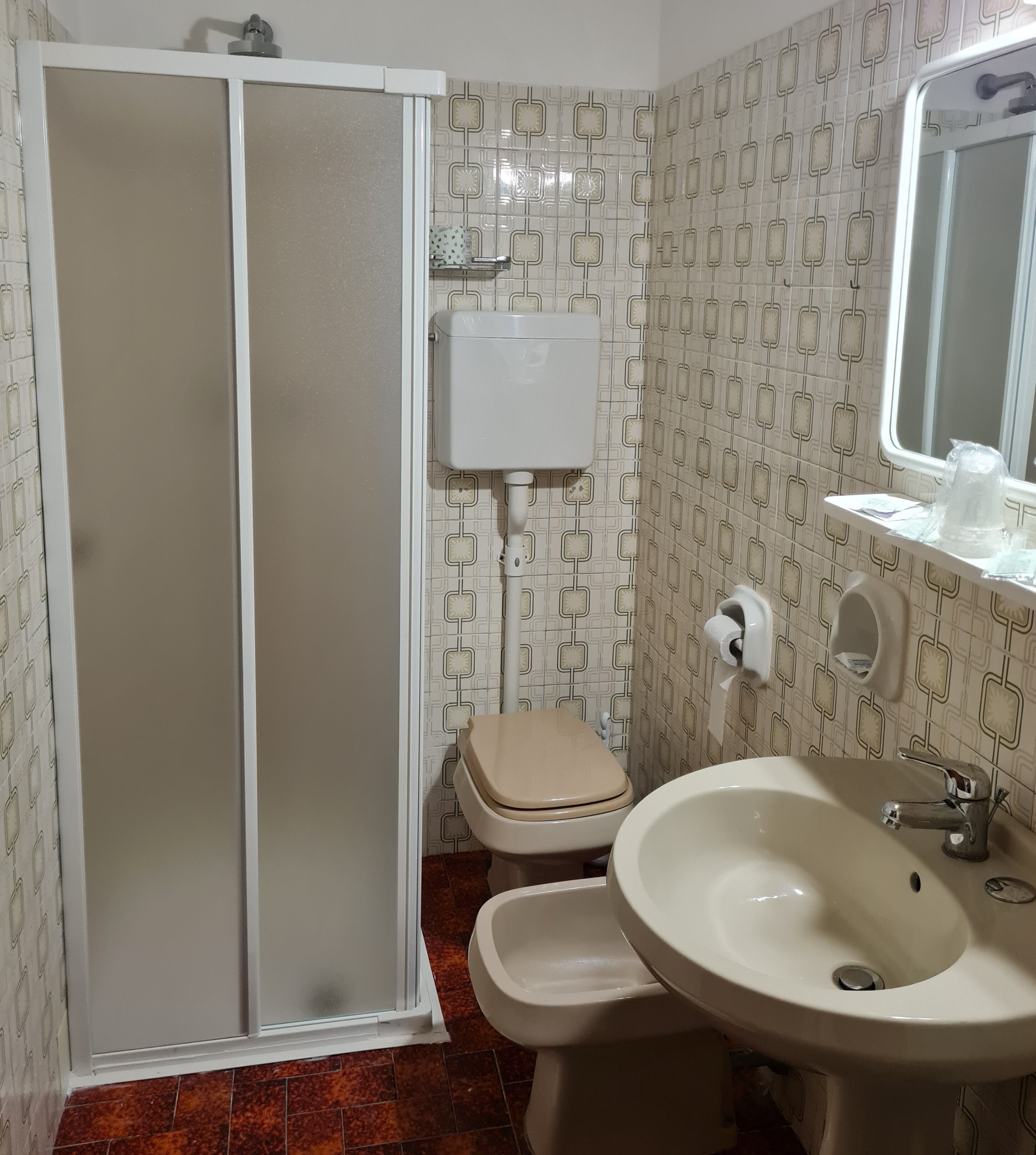 Baño con inodoro, bidé, lavamanos y ducha con puerta de vidrio.
